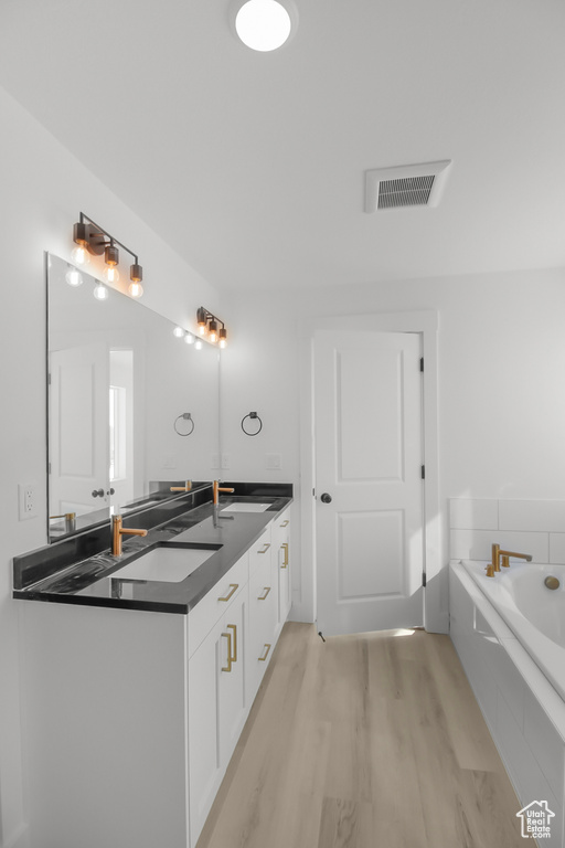 Bathroom featuring vanity, hardwood / wood-style floors, and a relaxing tiled tub