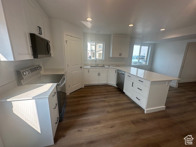 Kitchen with dark wood-type flooring, white cabinets, appliances with stainless steel finishes, and kitchen peninsula