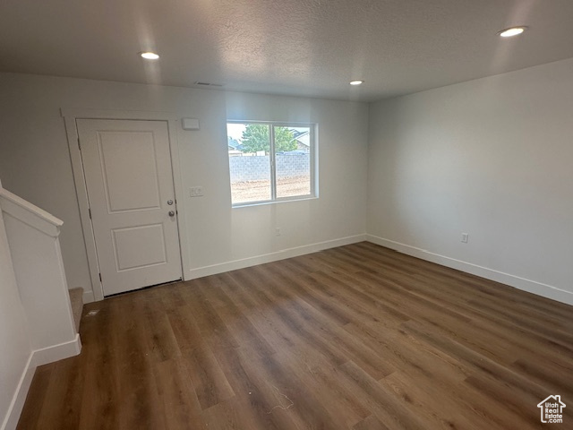 Empty room featuring dark wood-type flooring and a textured ceiling