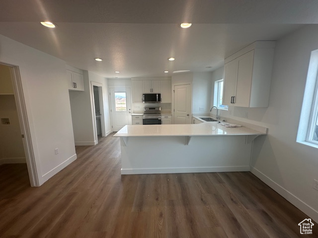 Kitchen featuring white cabinetry, kitchen peninsula, sink, dark hardwood / wood-style floors, and appliances with stainless steel finishes