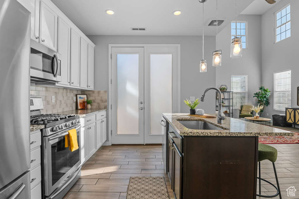 Kitchen featuring appliances with stainless steel finishes, light hardwood / wood-style floors, sink, white cabinetry, and plenty of natural light