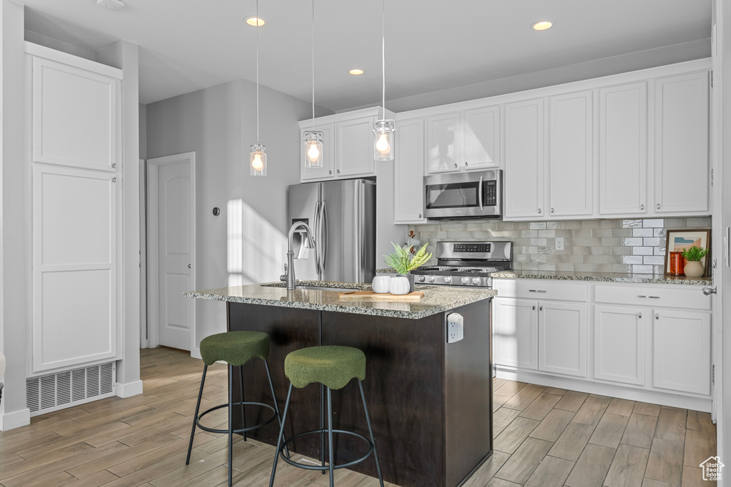 Kitchen with a center island with sink, light hardwood / wood-style floors, hanging light fixtures, stainless steel appliances, and white cabinets