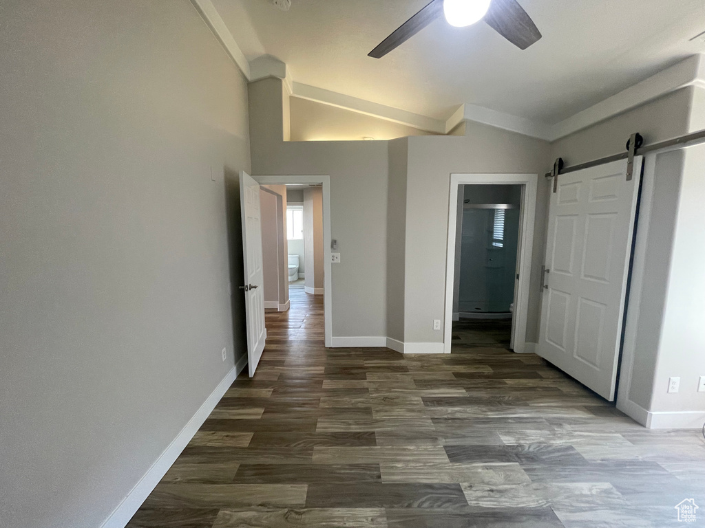 Unfurnished bedroom featuring vaulted ceiling, ceiling fan, dark wood-type flooring, and a barn door