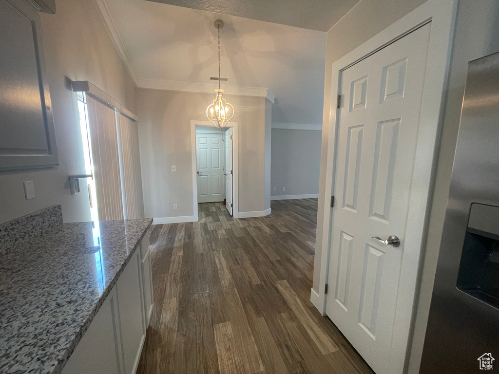 Kitchen with ornamental molding, decorative light fixtures, an inviting chandelier, light stone countertops, and dark wood-type flooring