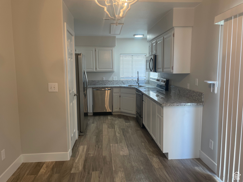 Kitchen with light stone counters, stainless steel appliances, a notable chandelier, white cabinetry, and dark hardwood / wood-style floors