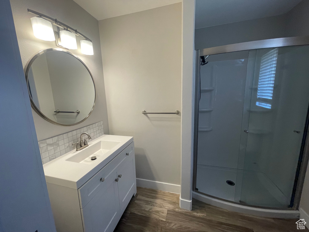 Bathroom featuring walk in shower, hardwood / wood-style flooring, tasteful backsplash, and vanity