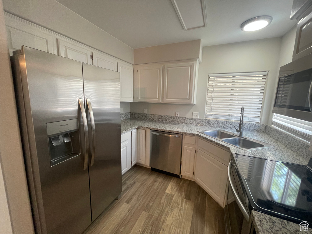 Kitchen featuring stainless steel appliances, sink, light stone countertops, white cabinets, and light hardwood / wood-style floors