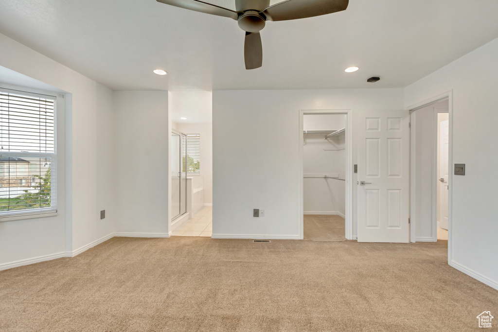 Unfurnished bedroom featuring light colored carpet, a walk in closet, a closet, ceiling fan, and connected bathroom