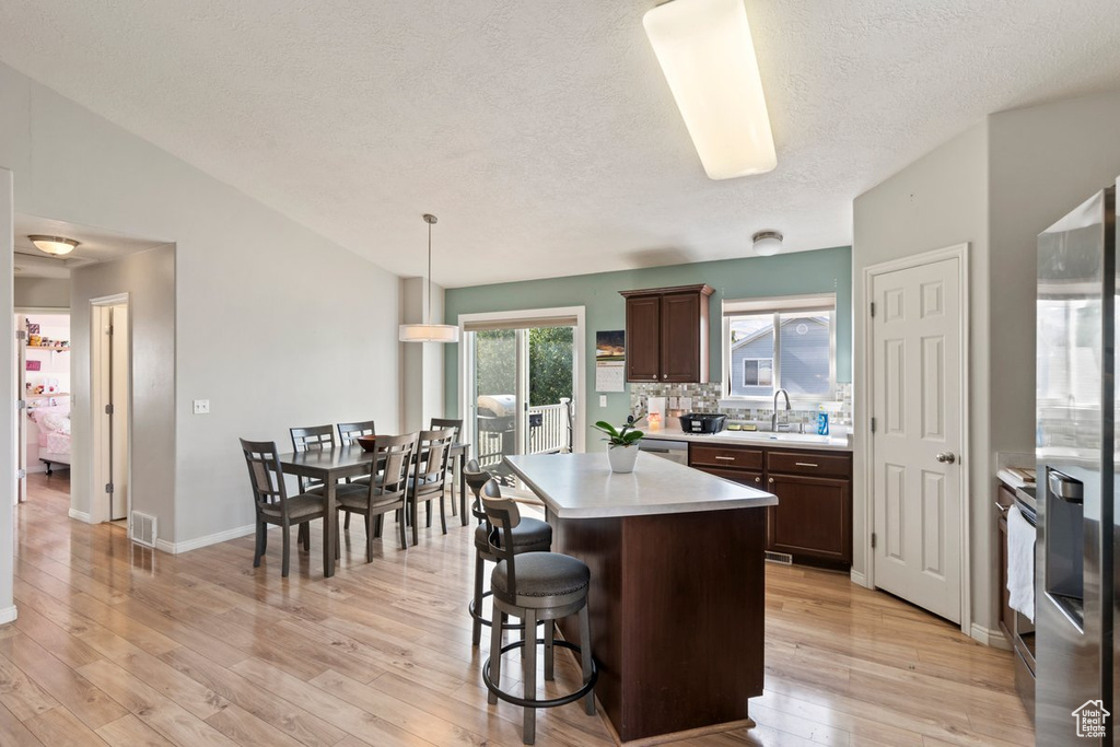 Kitchen with light wood-type flooring, decorative light fixtures, a kitchen island, and dark brown cabinets