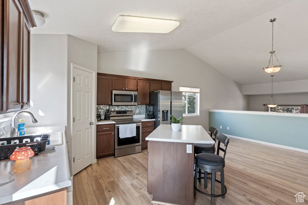 Kitchen featuring a kitchen island, pendant lighting, a kitchen bar, stainless steel appliances, and light wood-type flooring