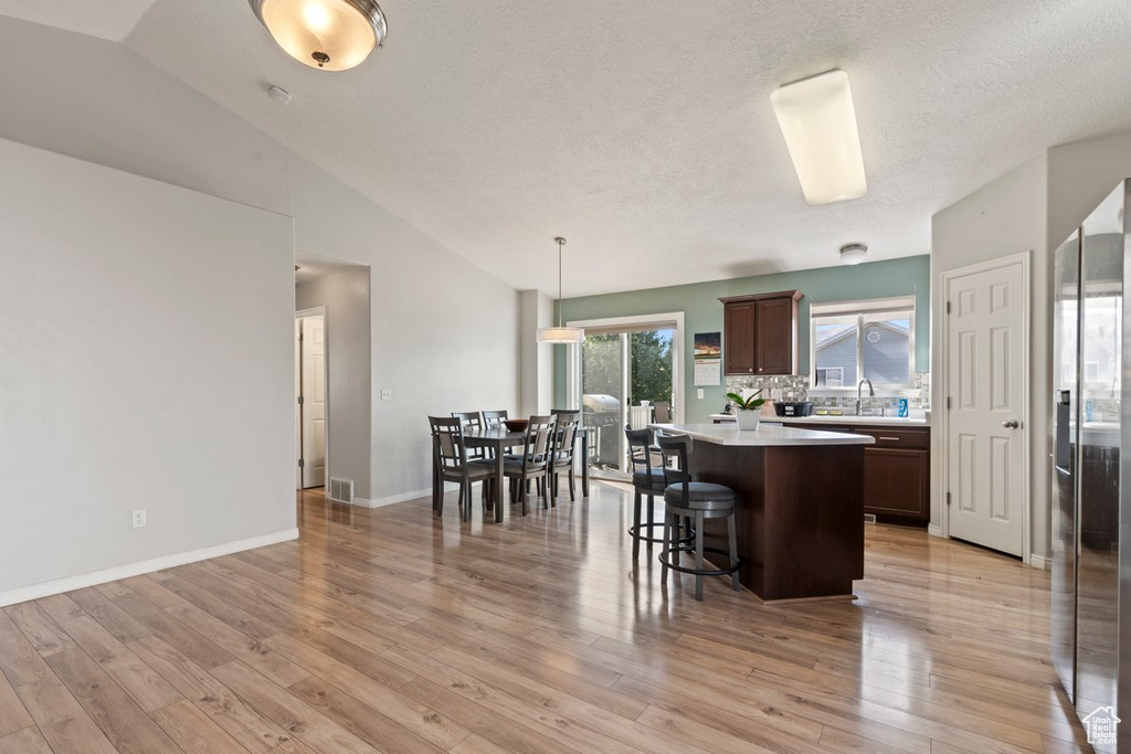 Kitchen featuring a kitchen island, dark brown cabinets, pendant lighting, light hardwood / wood-style floors, and lofted ceiling