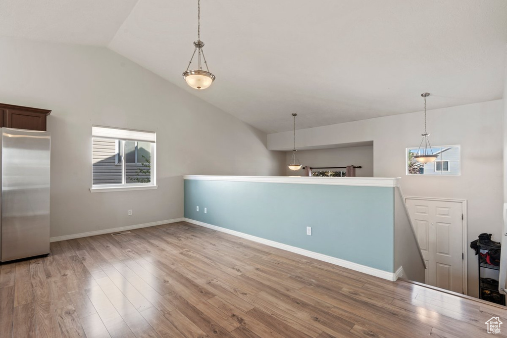 Kitchen with decorative light fixtures, hardwood / wood-style floors, stainless steel fridge, and vaulted ceiling