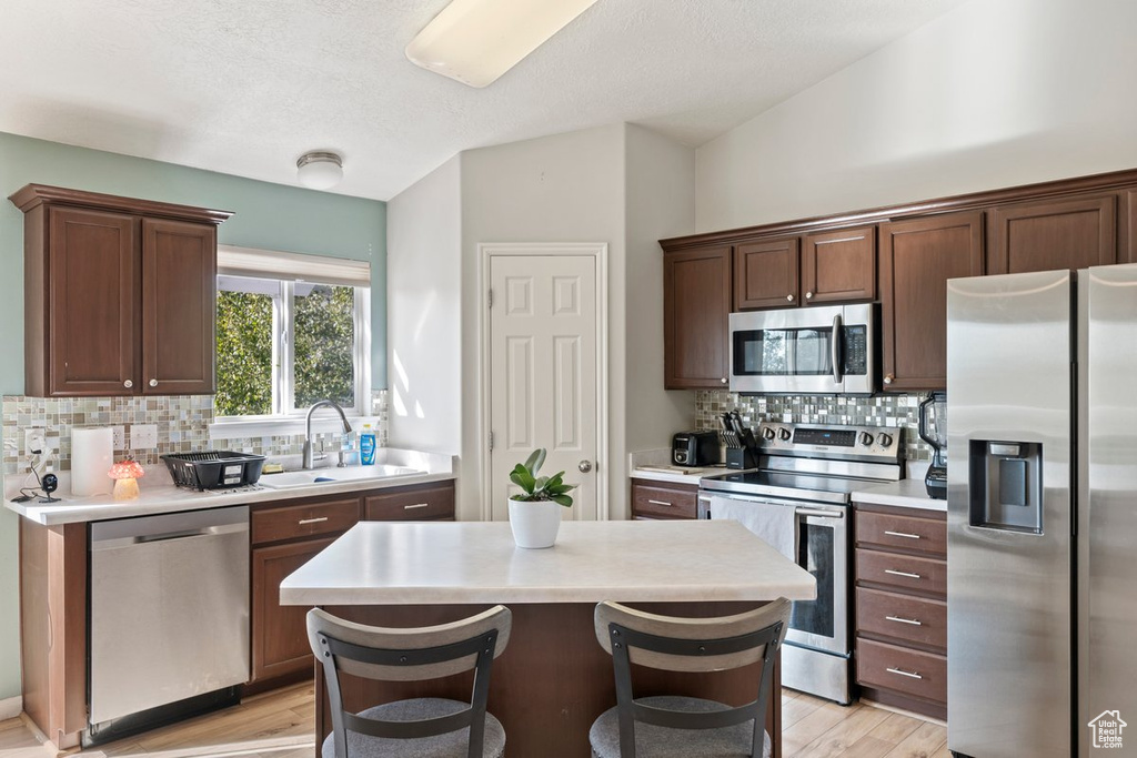 Kitchen with light hardwood / wood-style flooring, a center island, sink, appliances with stainless steel finishes, and a breakfast bar area