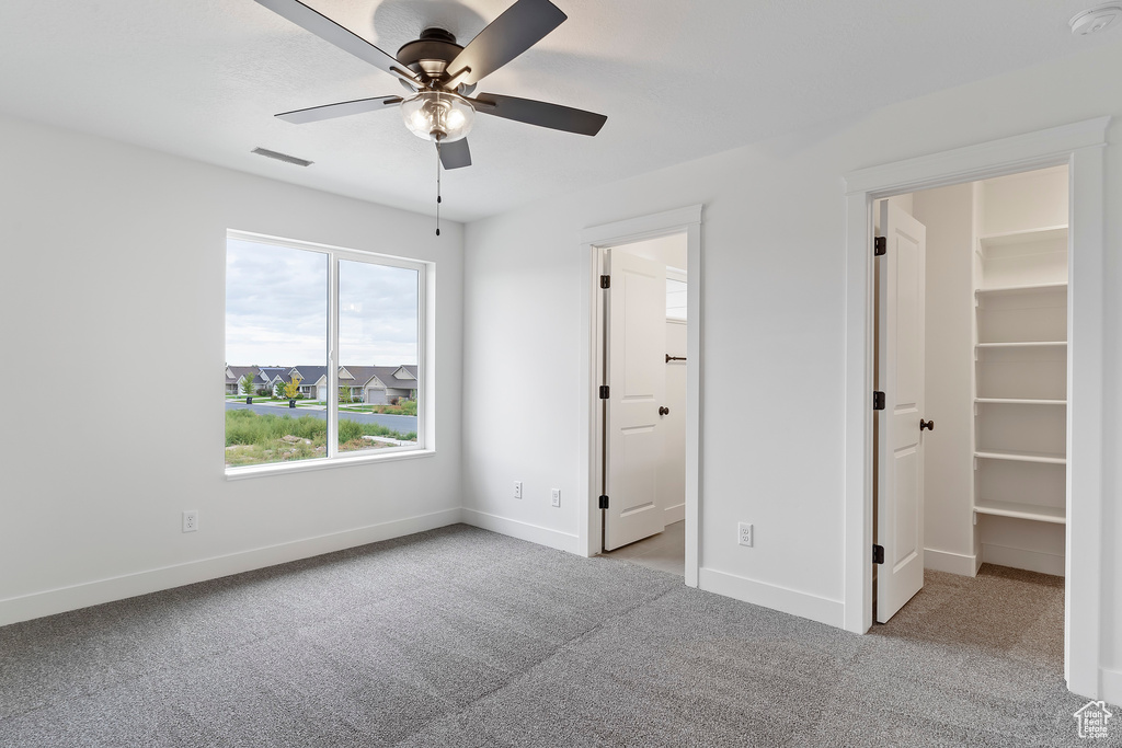 Unfurnished bedroom featuring light carpet, a walk in closet, ceiling fan, and a closet