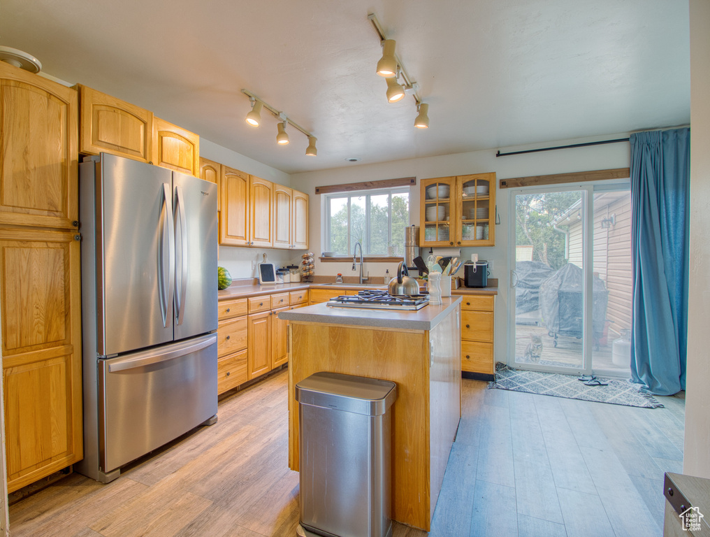 Kitchen featuring light brown cabinetry, light wood-type flooring, stainless steel appliances, track lighting, and a kitchen island