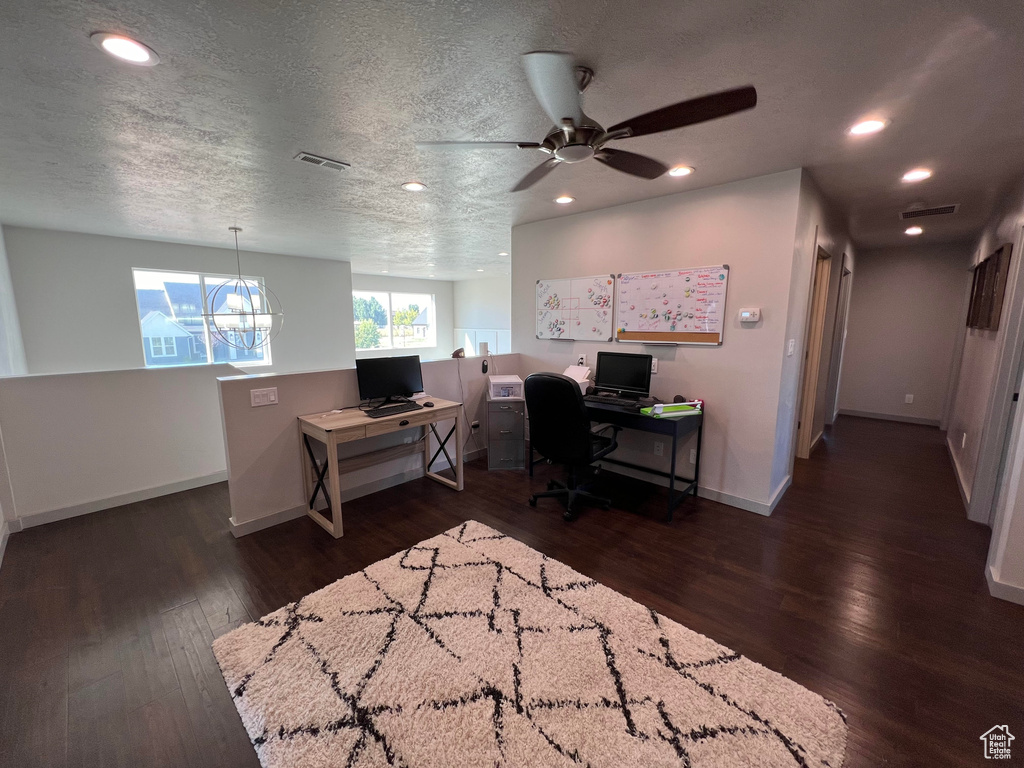 Office space with ceiling fan with notable chandelier, dark wood-type flooring, and a textured ceiling