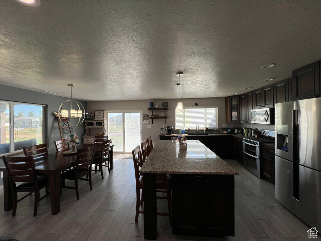 Kitchen with light wood-type flooring, a textured ceiling, a kitchen island, and stainless steel appliances