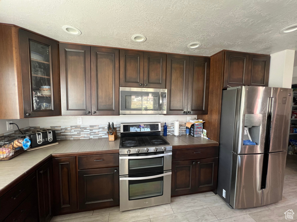 Kitchen featuring a textured ceiling, dark brown cabinetry, and appliances with stainless steel finishes