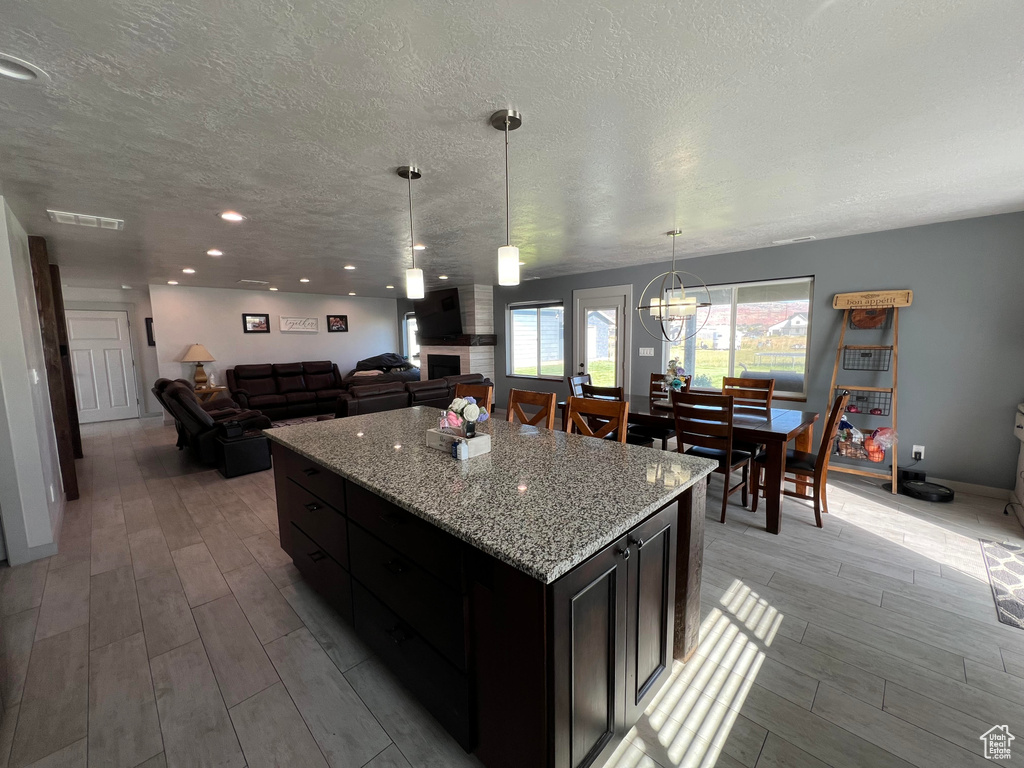 Kitchen with a center island, light wood-type flooring, light stone counters, pendant lighting, and a textured ceiling