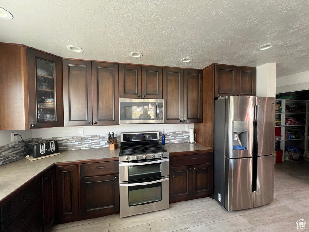 Kitchen with a textured ceiling, backsplash, dark brown cabinetry, and appliances with stainless steel finishes