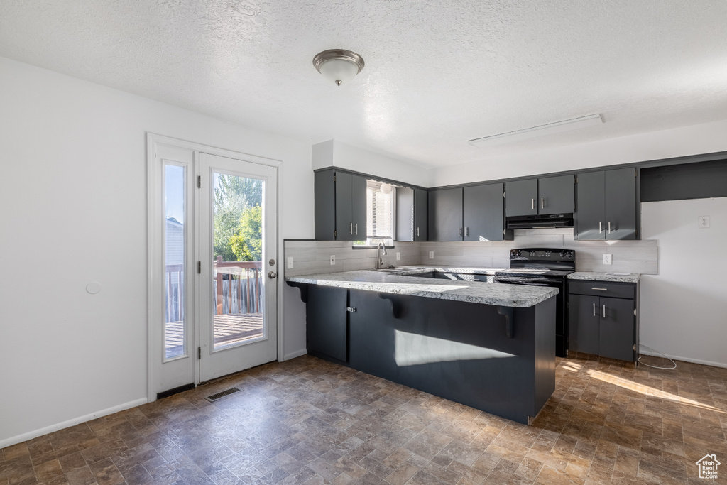 Kitchen featuring a textured ceiling, black / electric stove, kitchen peninsula, gray cabinets, and decorative backsplash