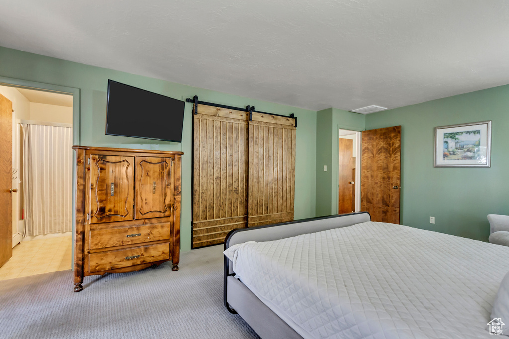 Bedroom with a barn door, ensuite bathroom, and light carpet