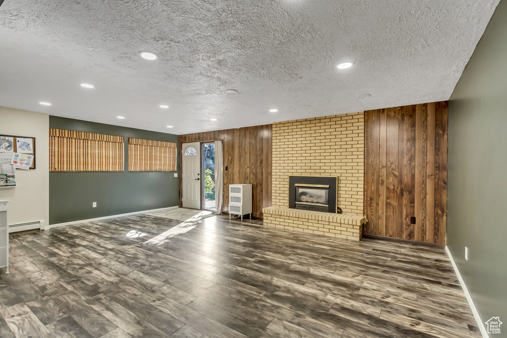 Unfurnished living room featuring a textured ceiling, a brick fireplace, wood walls, and dark hardwood / wood-style floors