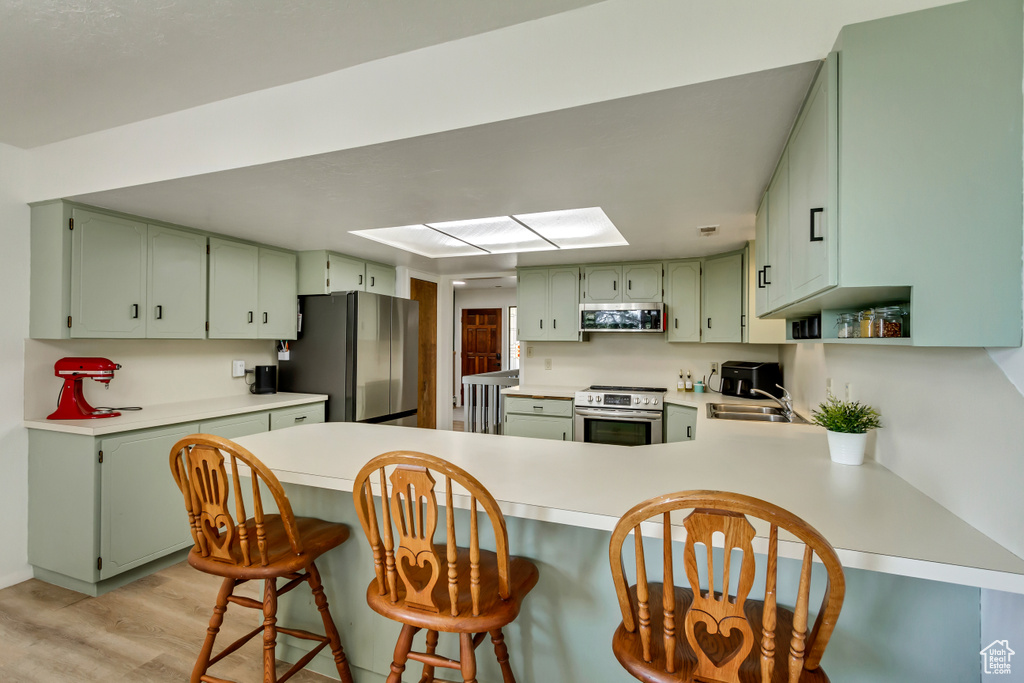 Kitchen with green cabinetry, stainless steel appliances, light hardwood / wood-style floors, and kitchen peninsula