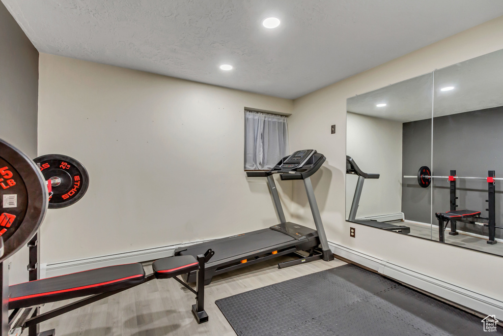 Exercise area with a baseboard radiator, light hardwood / wood-style floors, and a textured ceiling