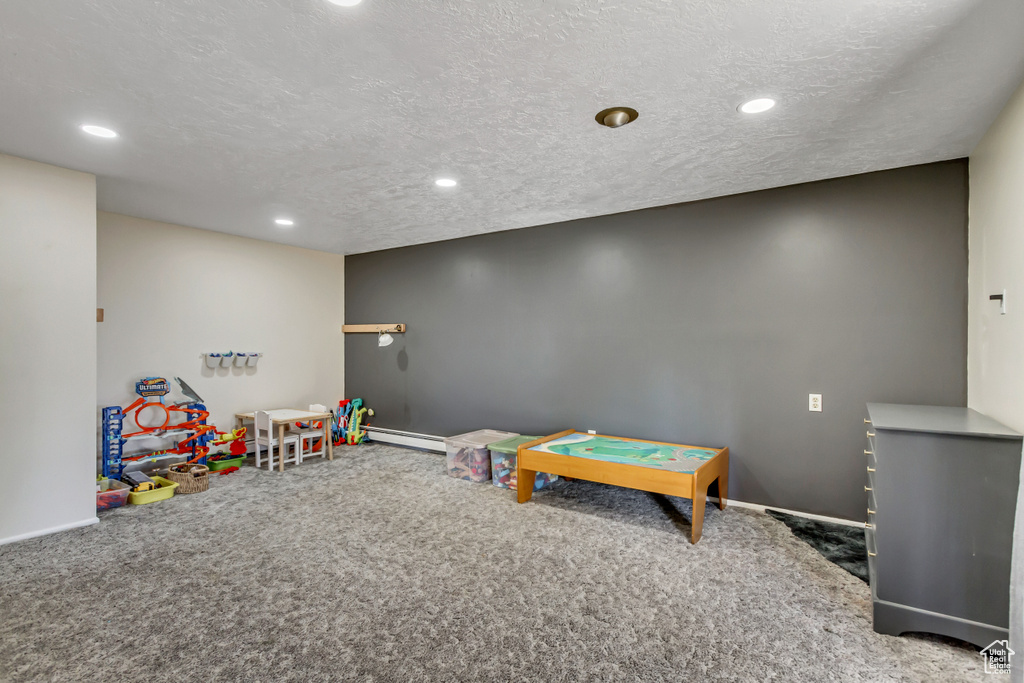 Recreation room featuring a textured ceiling, carpet flooring, and a baseboard heating unit