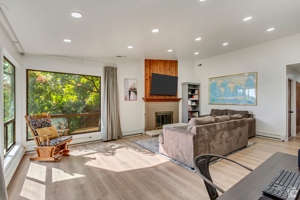 Living room with a fireplace, a healthy amount of sunlight, light hardwood / wood-style flooring, and a baseboard radiator