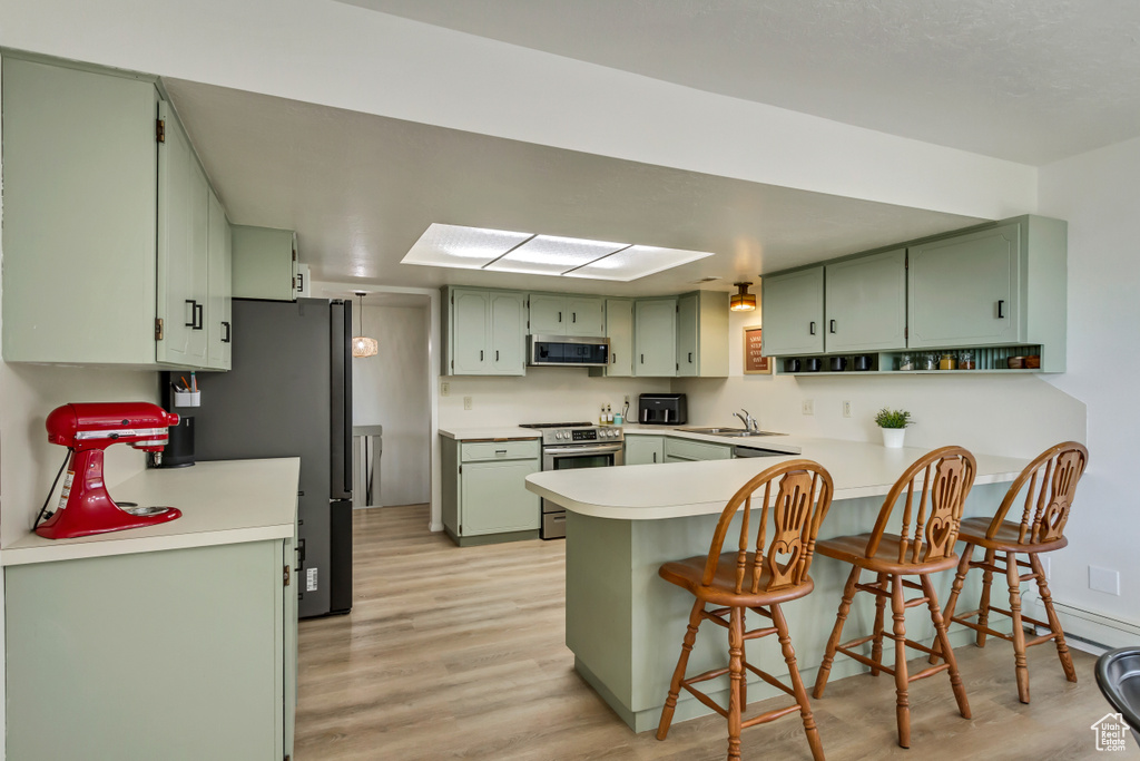 Kitchen featuring a kitchen breakfast bar, light hardwood / wood-style flooring, stainless steel appliances, kitchen peninsula, and green cabinetry