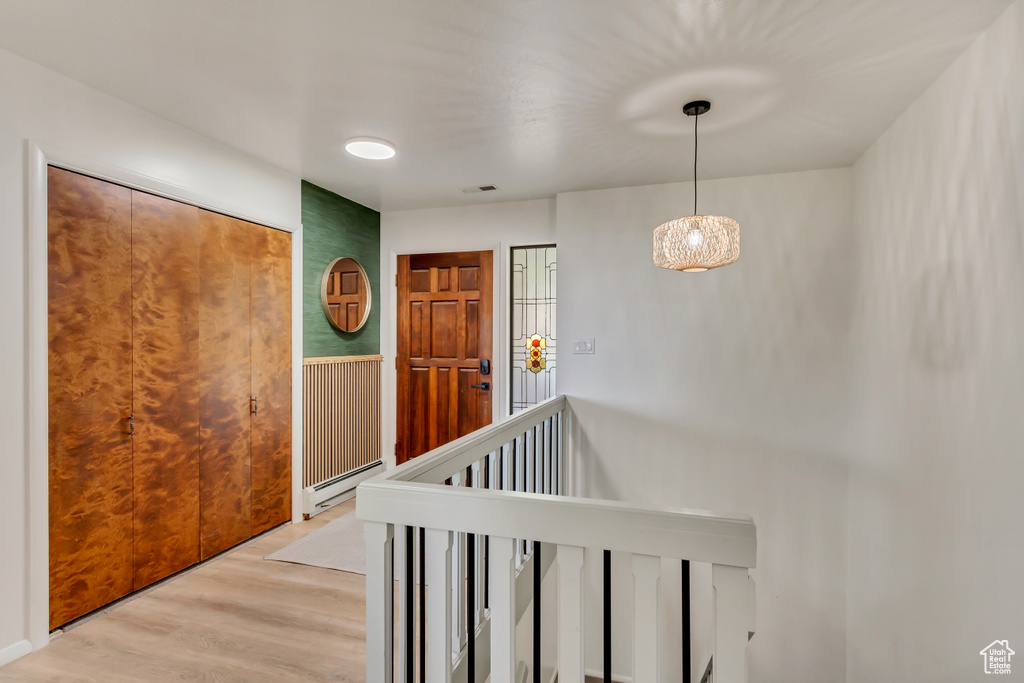 Corridor with a baseboard heating unit, an inviting chandelier, and light hardwood / wood-style floors