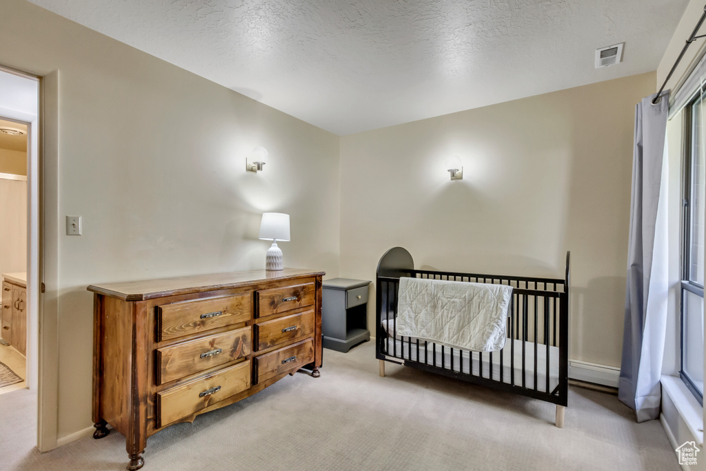 Carpeted bedroom featuring a textured ceiling, a nursery area, and a baseboard heating unit