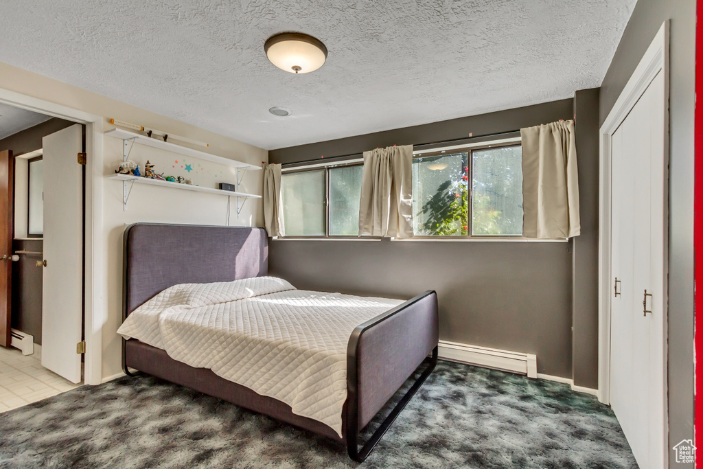 Carpeted bedroom featuring a baseboard heating unit and a textured ceiling