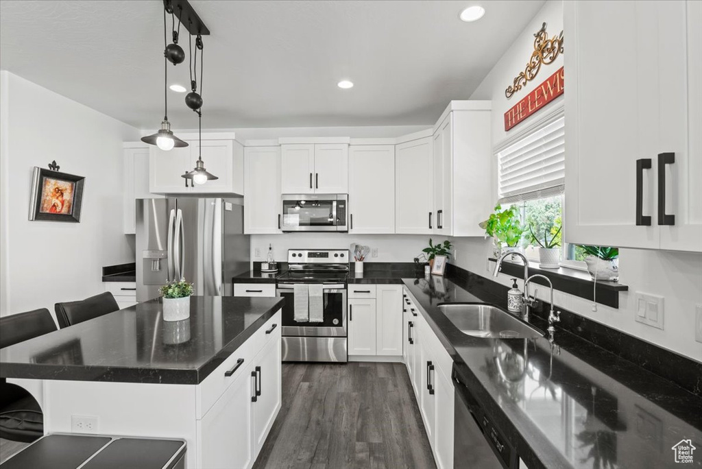 Kitchen featuring hanging light fixtures, stainless steel appliances, white cabinetry, sink, and dark hardwood / wood-style floors