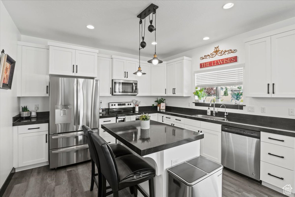 Kitchen featuring a center island, decorative light fixtures, appliances with stainless steel finishes, dark hardwood / wood-style flooring, and sink