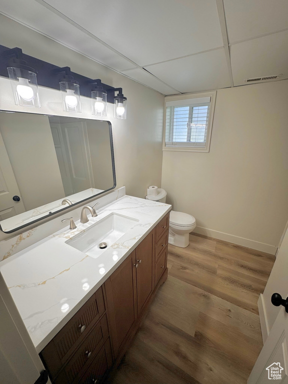 Bathroom featuring vanity, a drop ceiling, toilet, and wood-type flooring