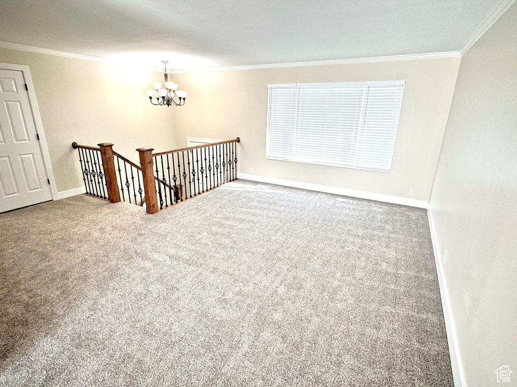 Carpeted empty room featuring ornamental molding and a chandelier