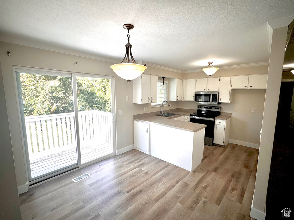 Kitchen with sink, white cabinetry, light hardwood / wood-style floors, stainless steel appliances, and decorative light fixtures