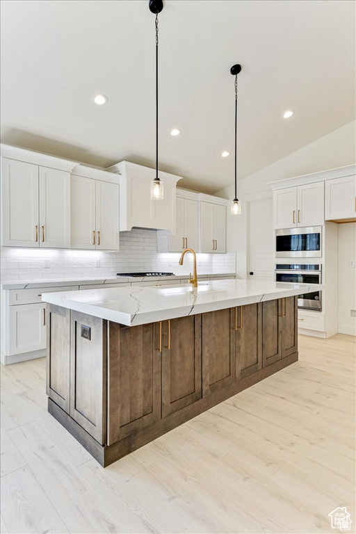 Kitchen featuring white cabinets, hanging light fixtures, light hardwood / wood-style flooring, lofted ceiling, and a large island