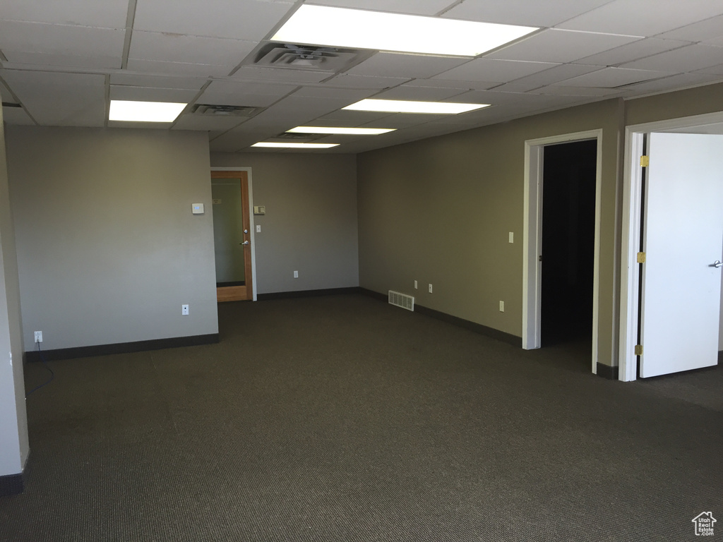 Unfurnished room featuring dark carpet and a drop ceiling