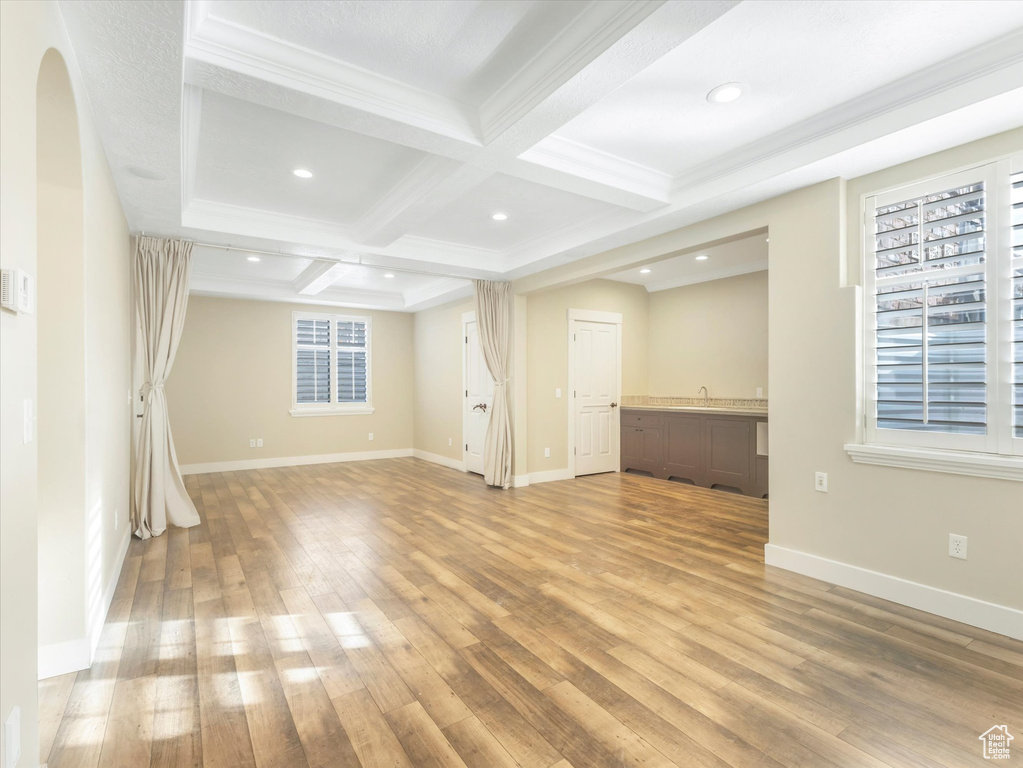 Unfurnished living room featuring beam ceiling, light wood-type flooring, crown molding, and coffered ceiling