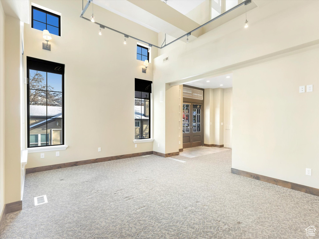 Carpeted empty room with track lighting, a towering ceiling, and french doors