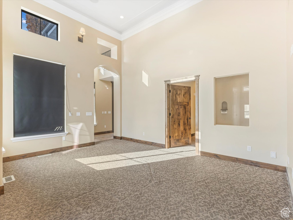 Unfurnished living room featuring carpet flooring, a towering ceiling, and ornamental molding