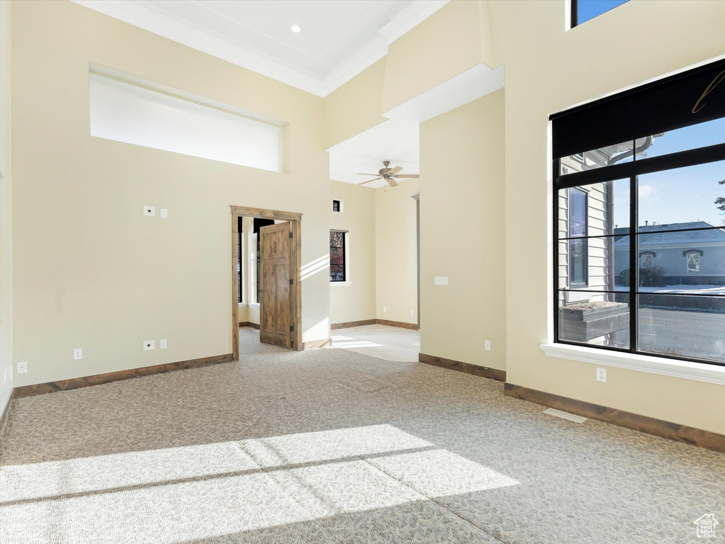 Carpeted empty room with a high ceiling, ceiling fan, and crown molding