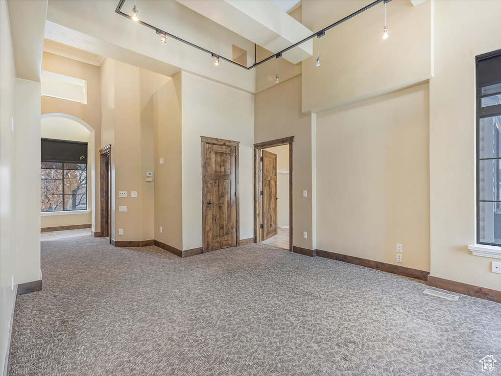 Carpeted spare room featuring a towering ceiling and rail lighting