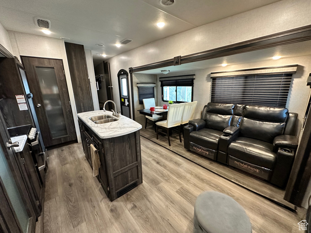 Interior space with light hardwood / wood-style flooring, dark brown cabinetry, a kitchen island with sink, and sink