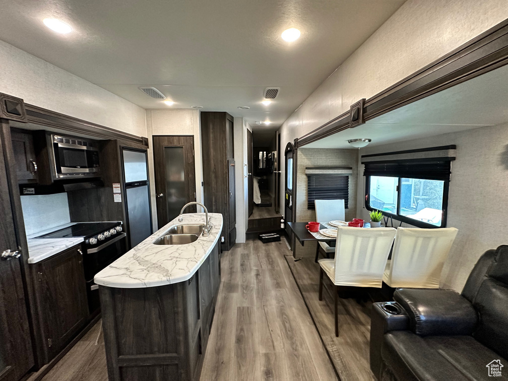 Kitchen featuring light hardwood / wood-style floors, an island with sink, sink, electric stove, and stainless steel microwave