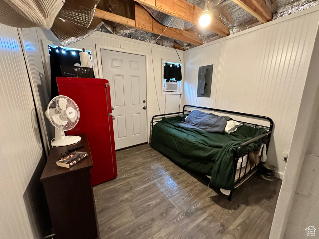 Bedroom featuring electric panel, beam ceiling, hardwood / wood-style flooring, and wooden walls